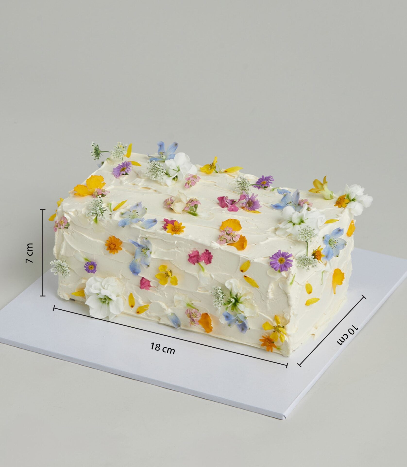 White buttercream layer cake adorned with edible flowers in yellow, pink, purple, and blue petals