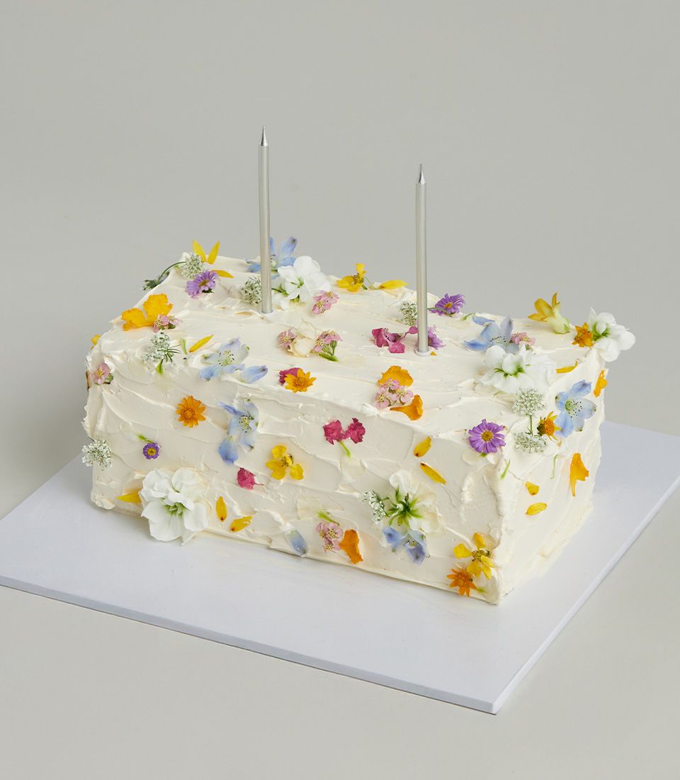 Vanilla layer cake with textured white buttercream frosting topped with colorful edible flowers and silver candles