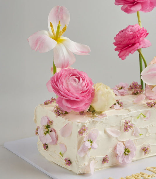 Romantic white buttercream layer cake topped with fresh pink ranunculus, tulips, and roses
