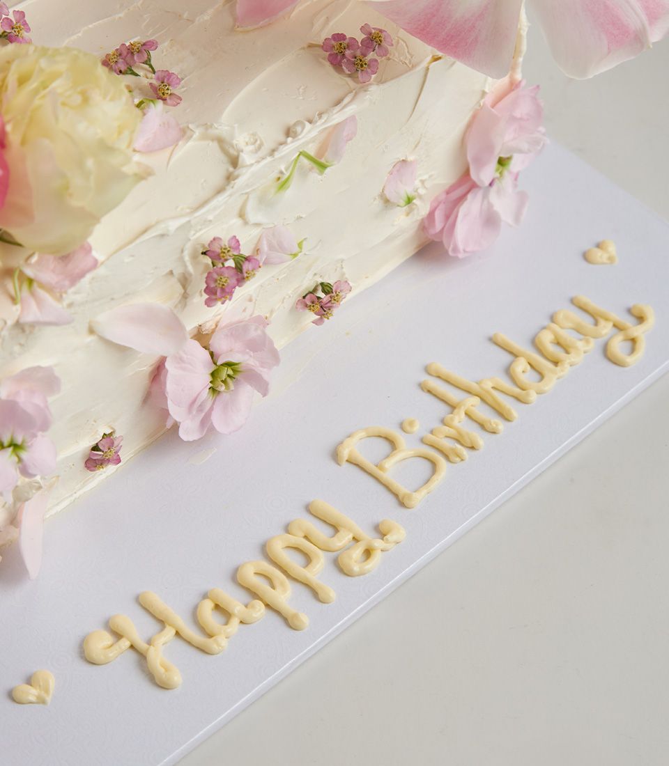 Romantic whimsical layer cake with cream frosting, fresh edible flowers in pink and yellow, artisan celebration baking