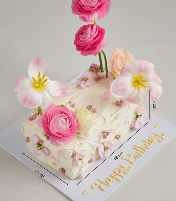 Cream buttercream layer cake adorned with fresh pink ranunculus, tulips, and edible flowers for celebrations