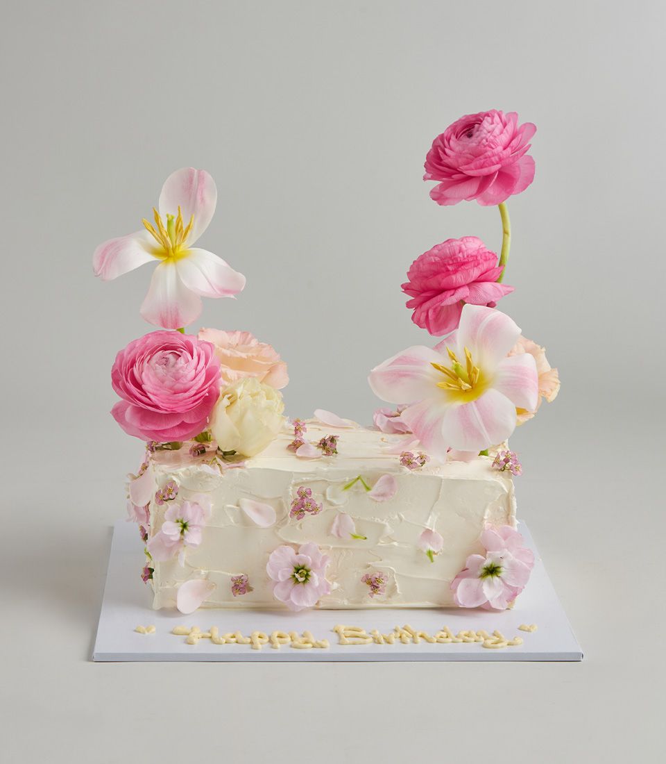 White buttercream layer cake topped with fresh pink tulips, ranunculus, and edible flowers