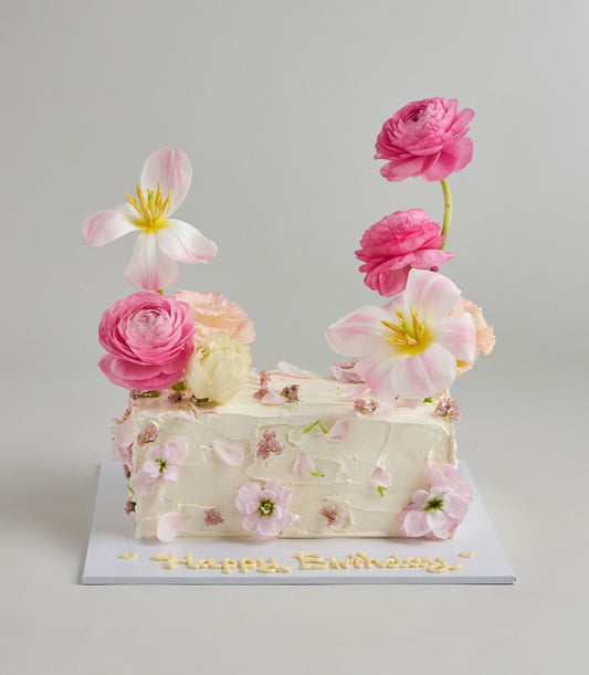 White buttercream layer cake topped with fresh pink tulips, ranunculus, and edible flowers