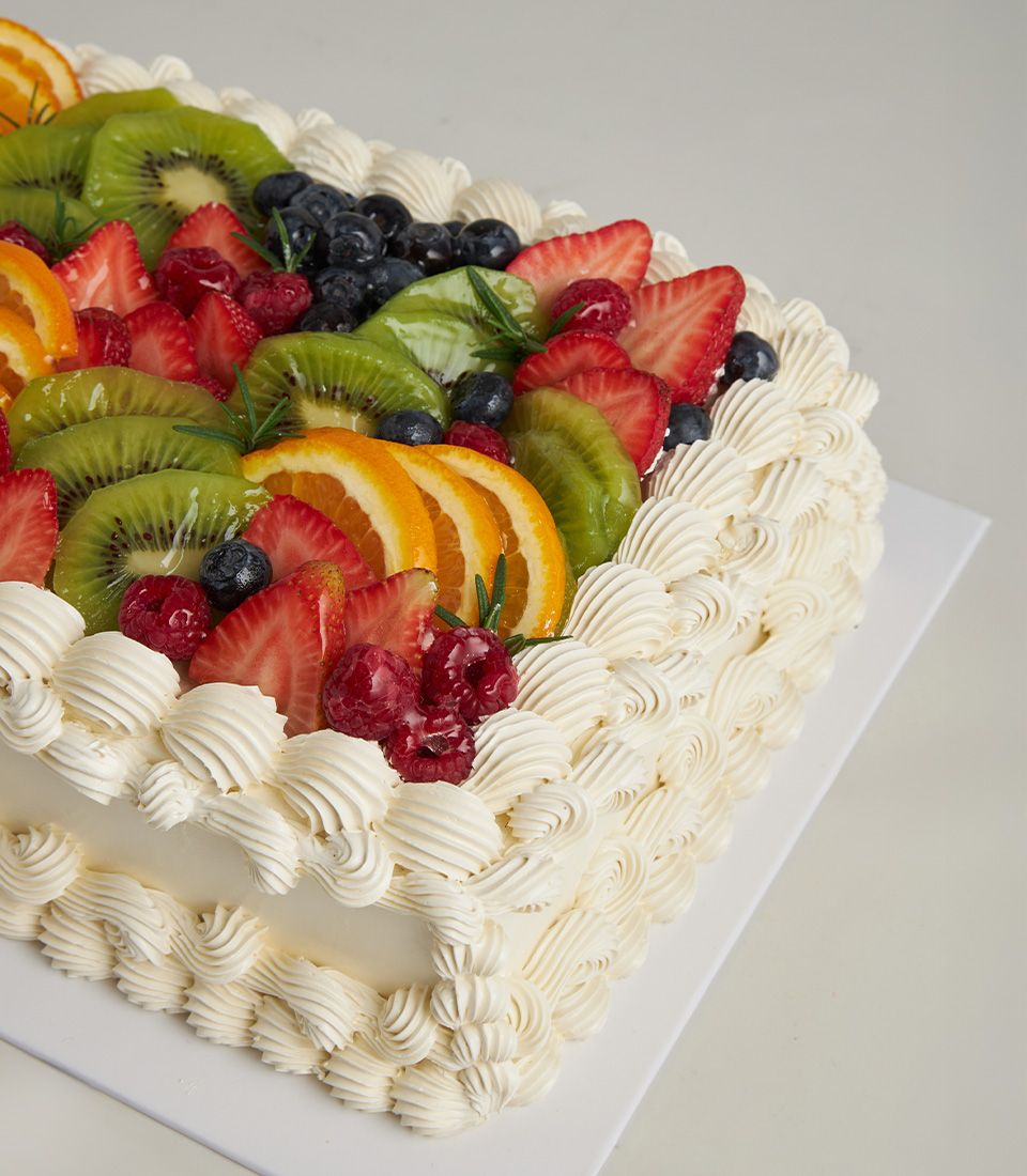 Luxury fresh fruit celebration cake with strawberries, kiwi, and berries atop white cream frosting
