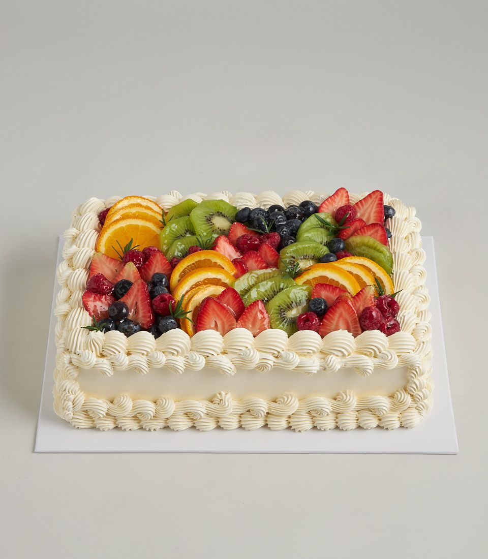 Strawberry and fresh fruit layer cake with kiwi, blueberries, and raspberries, topped with rosemary sprigs and white cream
