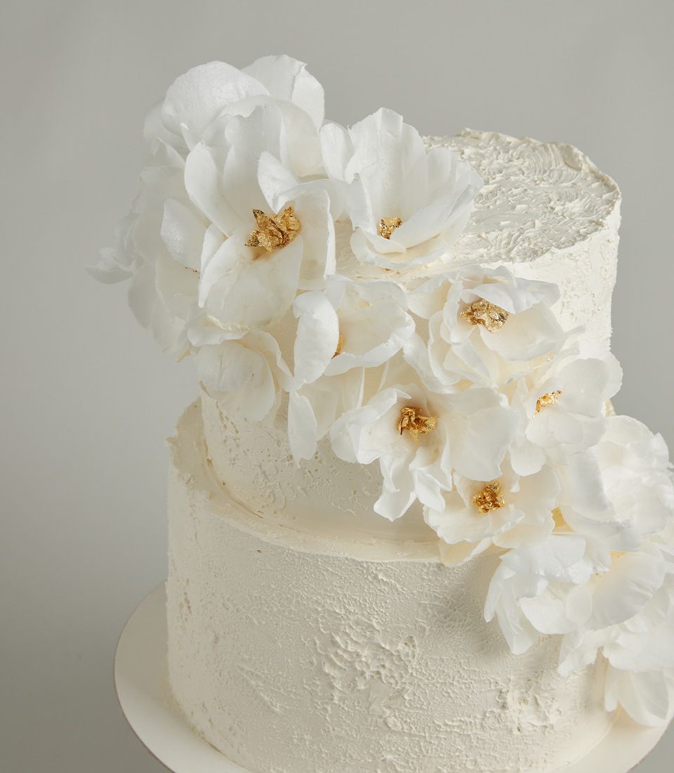 Two-tier white wedding cake with textured buttercream and cascading edible wafer flowers with gold leaf centers