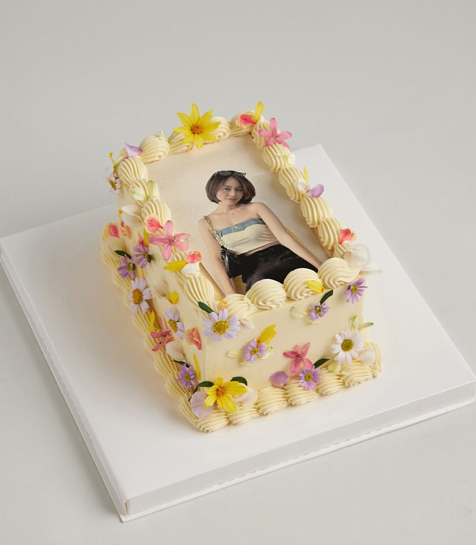 Personalised rectangular cake with edible photo of woman, vanilla frosting, piped swirls and fresh yellow, pink, purple