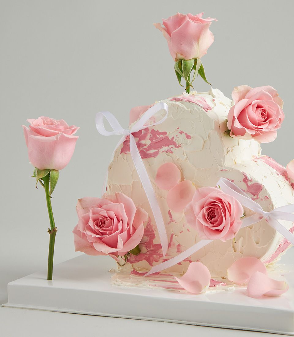 Heart-shaped layer cake with white frosting, pink roses, and romantic white ribbons for celebrations