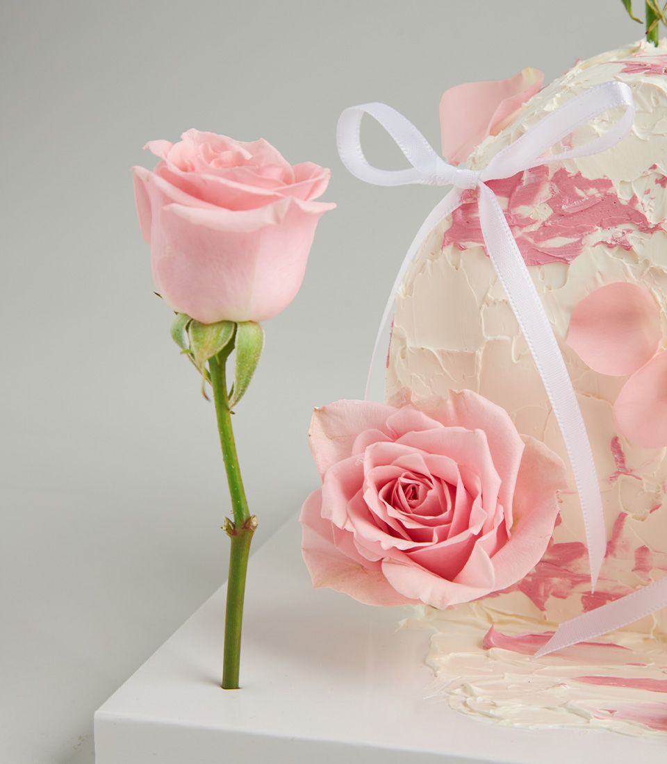 Pink rose and strawberry layer cake with white frosting, fresh petals, and ribbon bow for romantic gifting