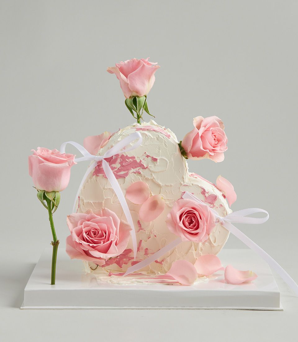 Heart-shaped strawberry cake with fresh pink roses and white ribbons
