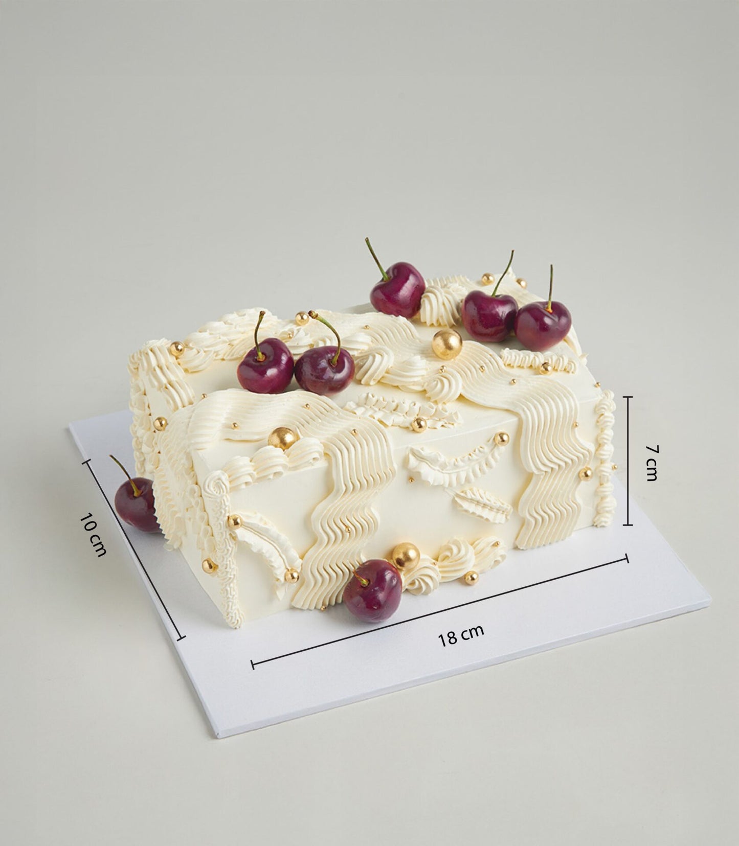 Luxury rectangular cherry cream cake with white frosting swirls, golden pearls and fresh dark red cherries on white board