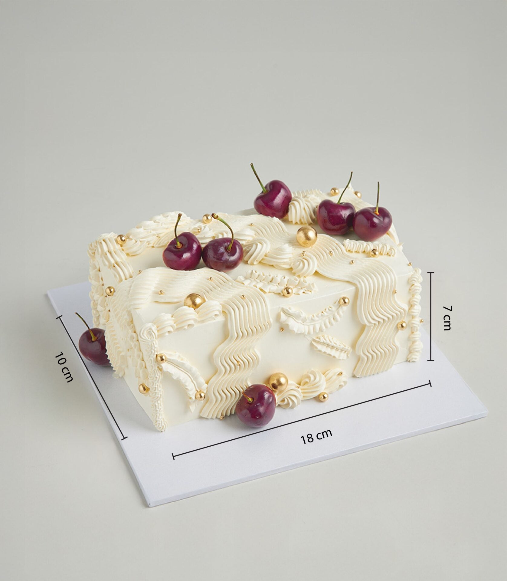Luxury rectangular cherry cream cake with white frosting swirls, golden pearls and fresh dark red cherries on white board