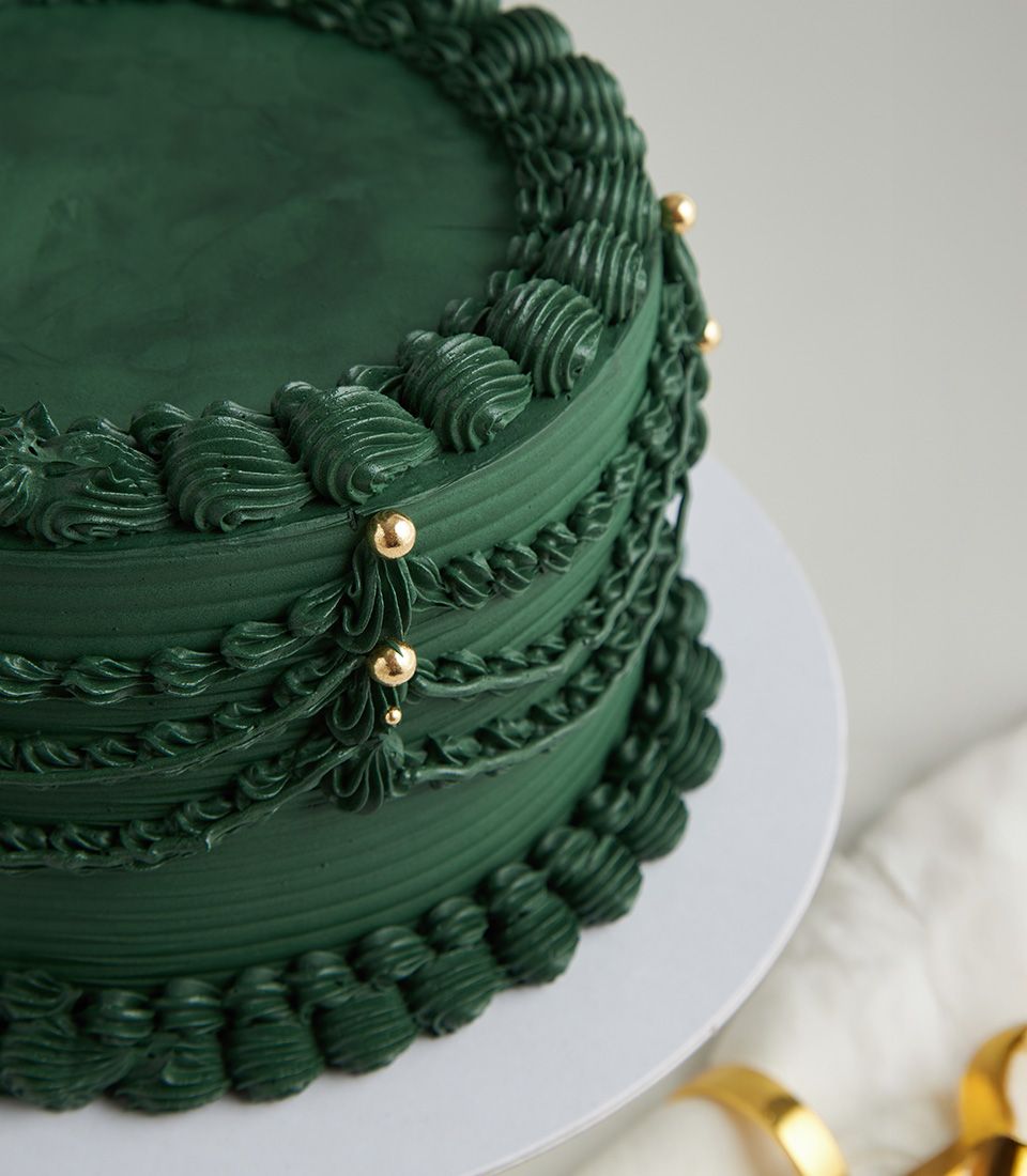 Charlotte Bakery artisan cake: Emerald green buttercream, draped piping detail, and gold pearls. Order your custom cake in Bangkok today!