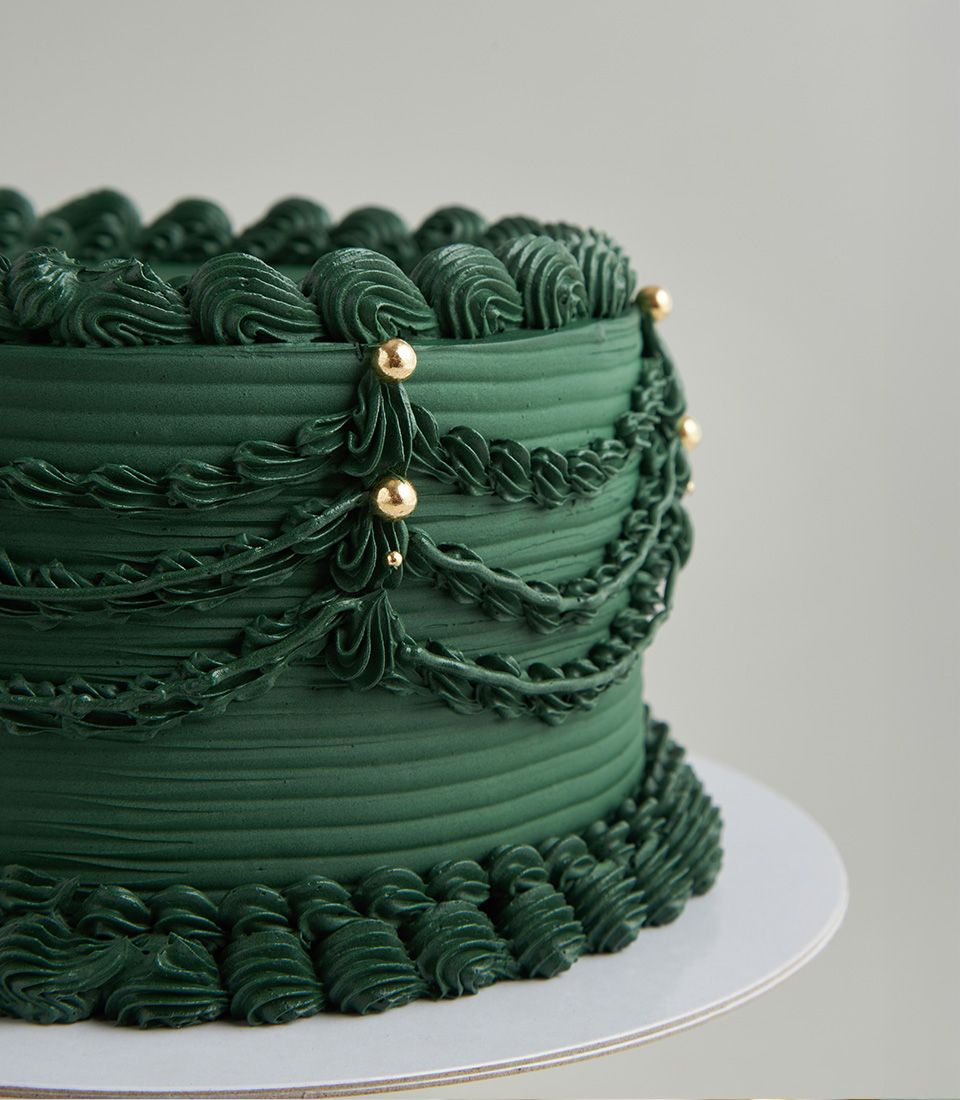 Artisan emerald green buttercream cake from Charlotte Bakery, Bangkok. Vintage piped details and gold pearl accents; order custom cake Bangkok.