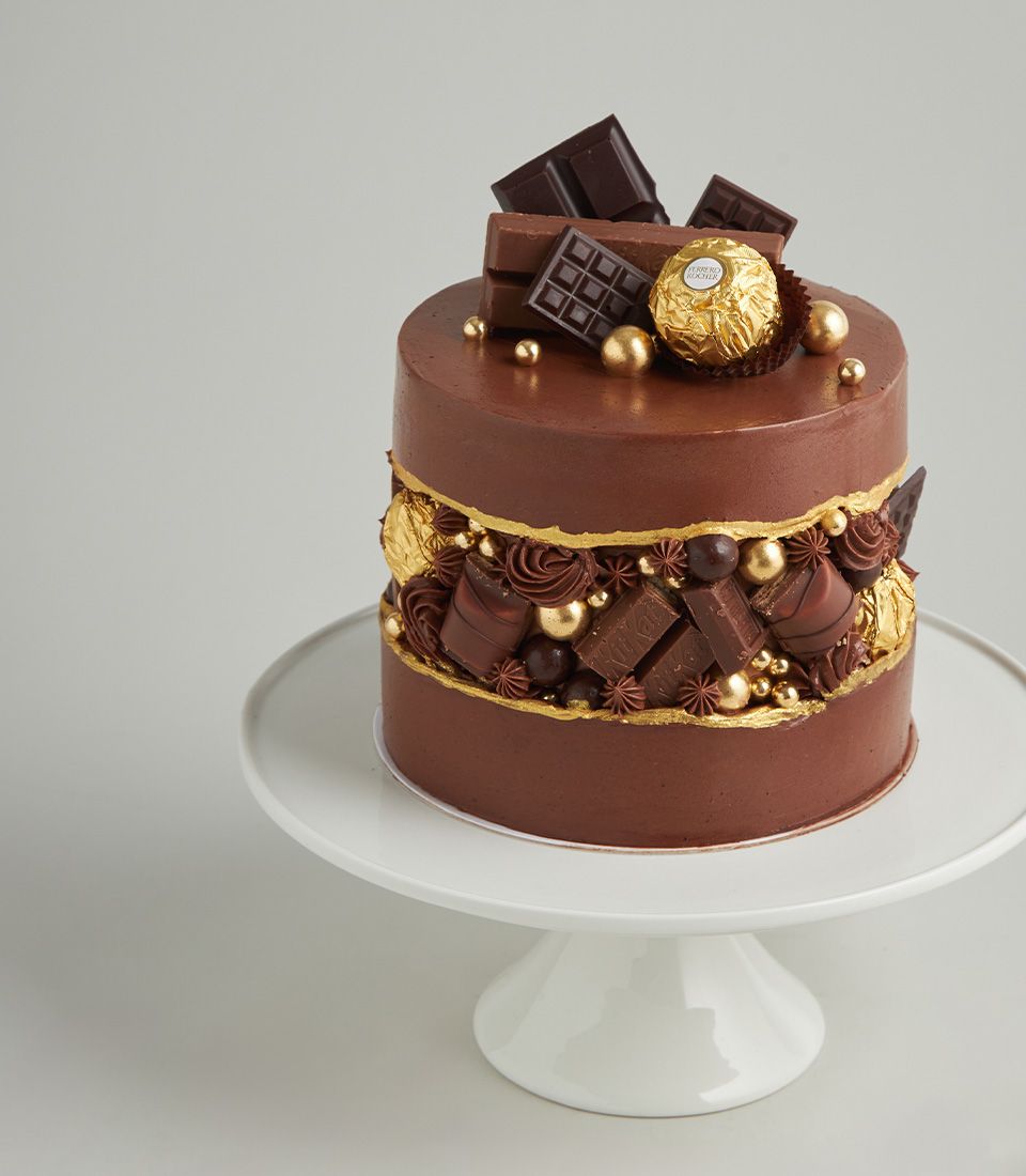 Luxe two-tiered chocolate cake with Ferrero Rocher, dark chocolate bars, and gold leaf on ceramic stand
