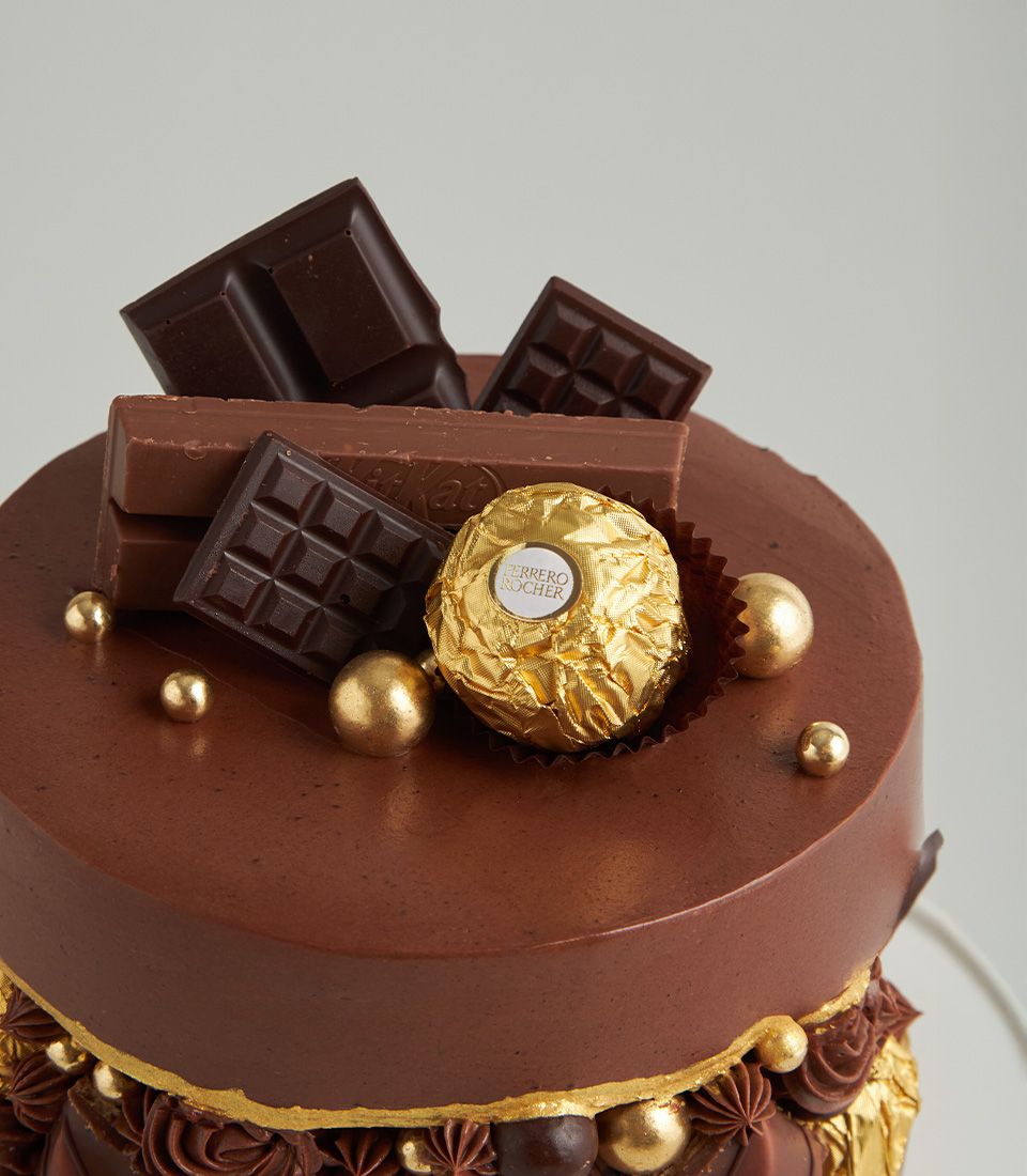 Decadent two-tier chocolate cake topped with Ferrero Rocher, dark chocolate bars, and edible gold pearls