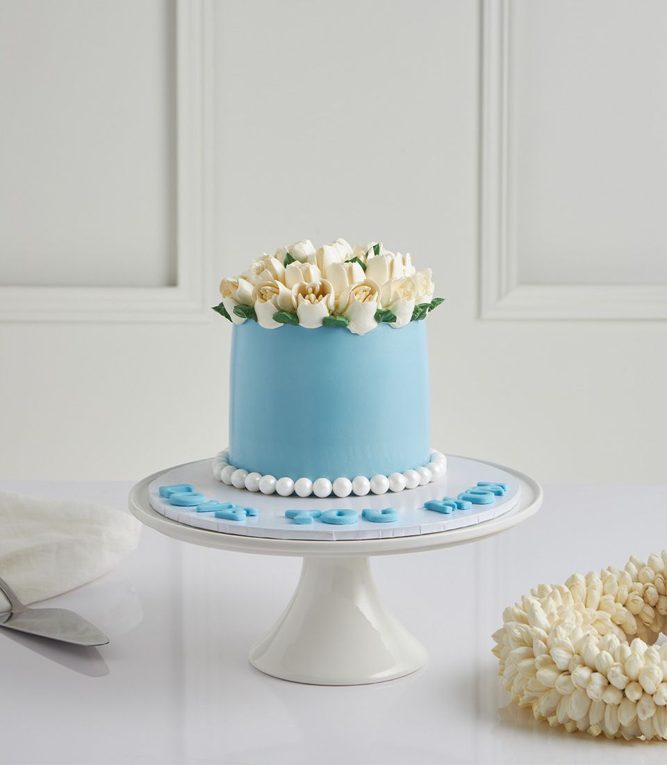 Light blue Mother's Day cake with white jasmine buttercream flowers and pearl trim on cake stand