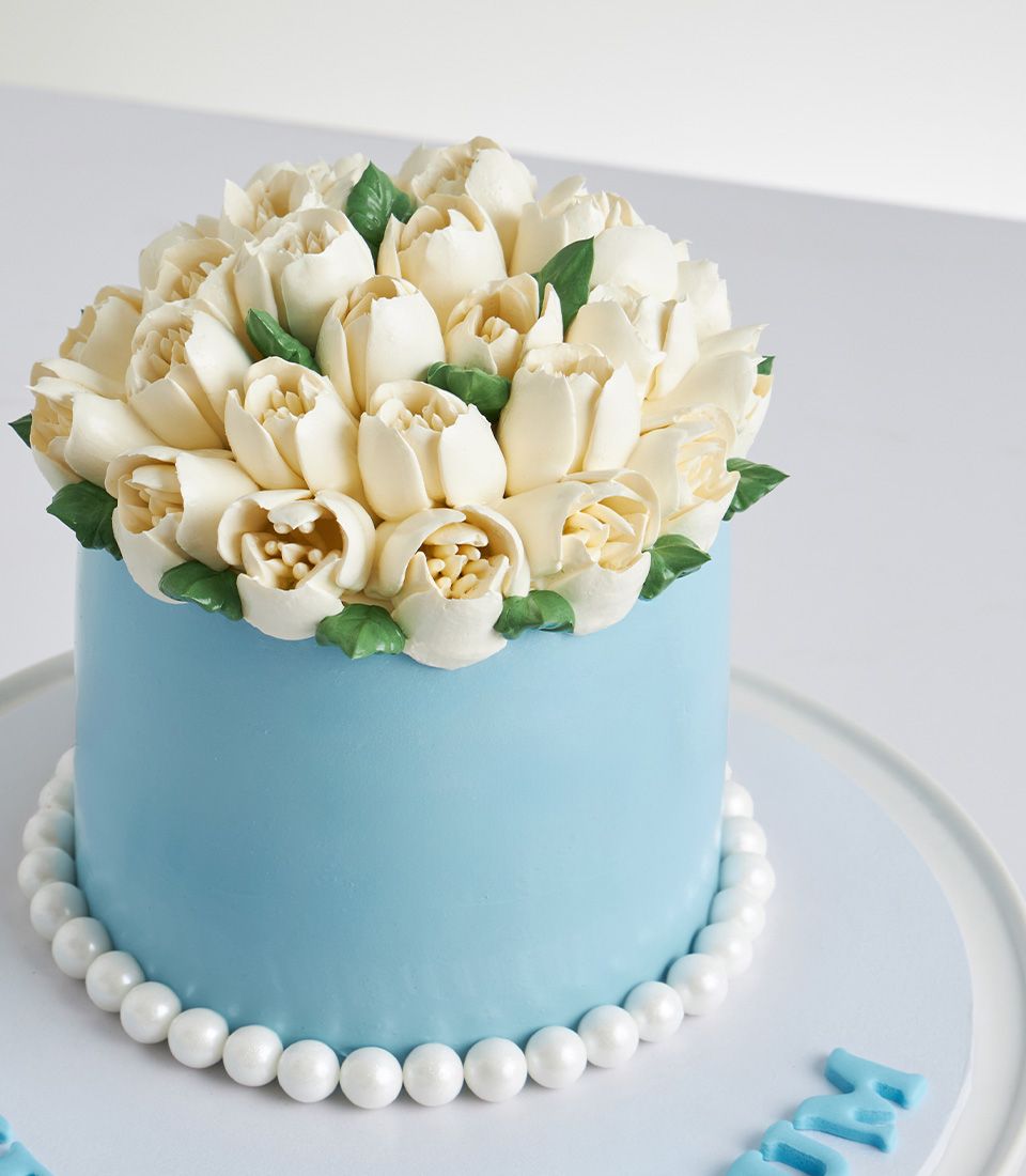 Light blue Mother's Day cake with white buttercream flowers and edible pearls from Charlotte Bakery