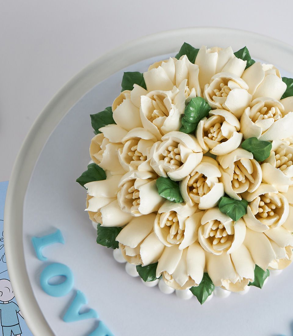 Vanilla Jasmine Mother's Day cake with cream buttercream flowers and green leaves on light blue board