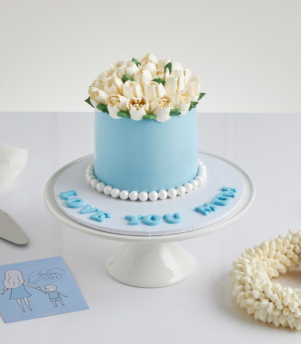 Light blue vanilla jasmine Mother's Day cake with white buttercream tulips, pearl trim, and "Love You Mum" message on cake