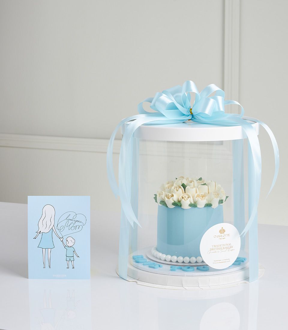 Light blue vanilla jasmine Mother's Day cake with white floral frosting, pearls, and "Happy Mom" lettering in gift box with
