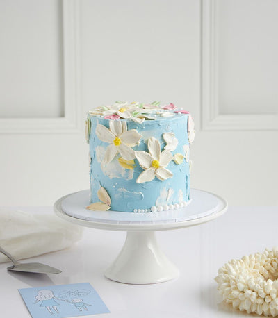 Light blue coconut cake with white buttercream flowers and pearls on ceramic stand, Mother's Day gift