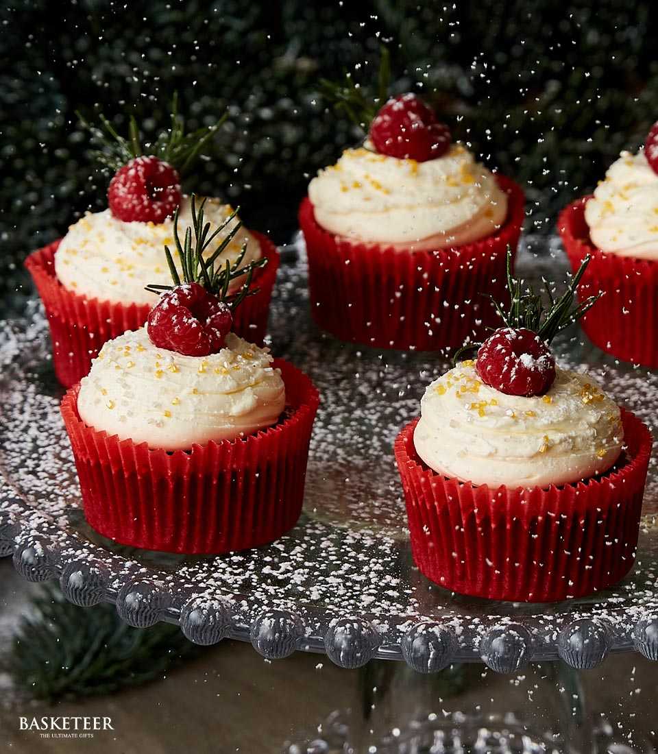 Red raspberry Christmas cupcakes with white frosting and golden sprinkles on beaded glass stand
