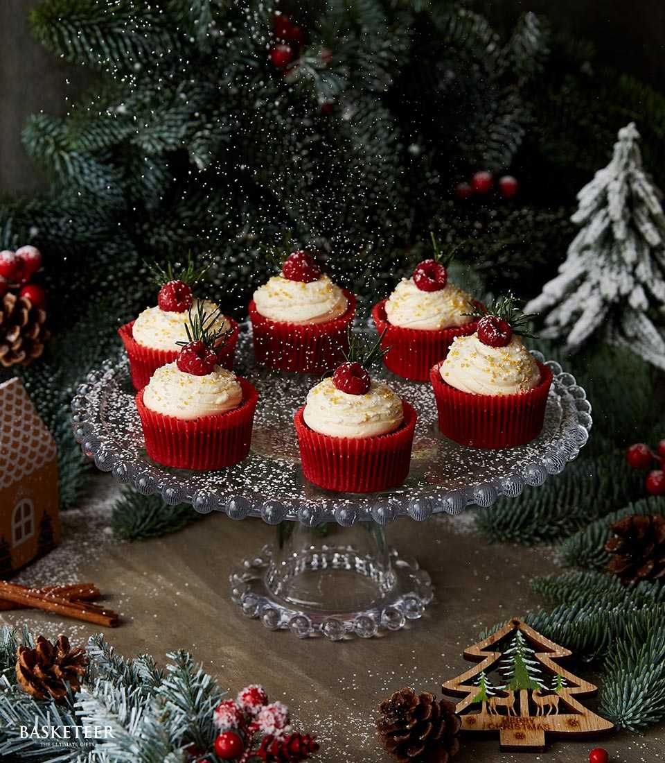 Red velvet Christmas cupcakes with white frosting, fresh raspberries, and gold dust on glass stand with festive holiday