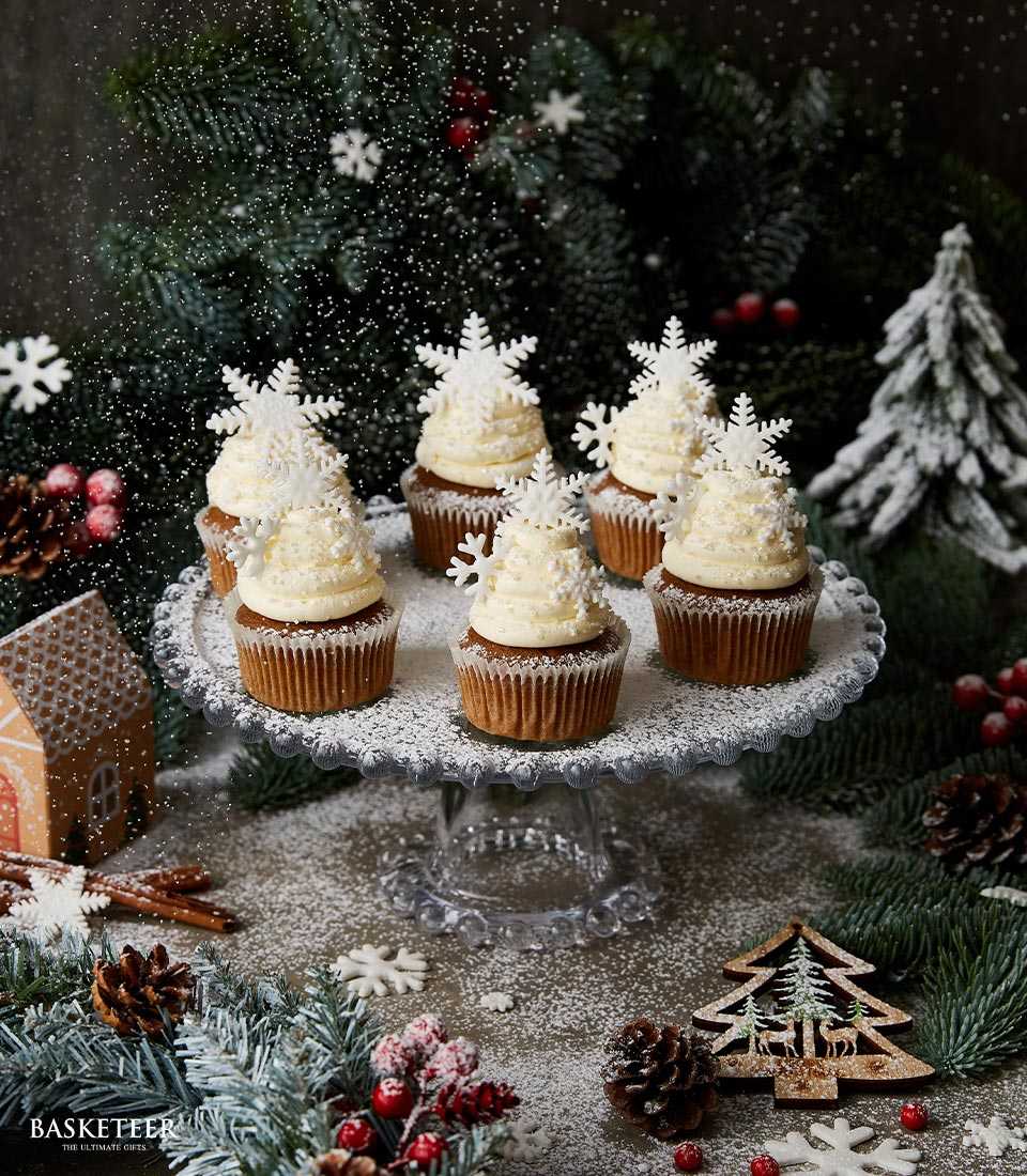 Snowflake vanilla cupcakes with white frosting and powdered sugar on glass cake stand, festive Christmas gift set