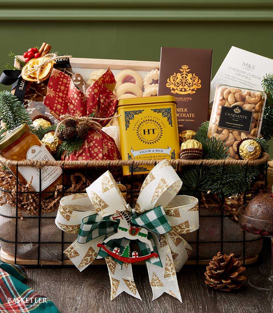 Festive dark metal mesh gift basket with gourmet cookies, mango jam, herbal tea, chocolate, and cashews, decorated with pine