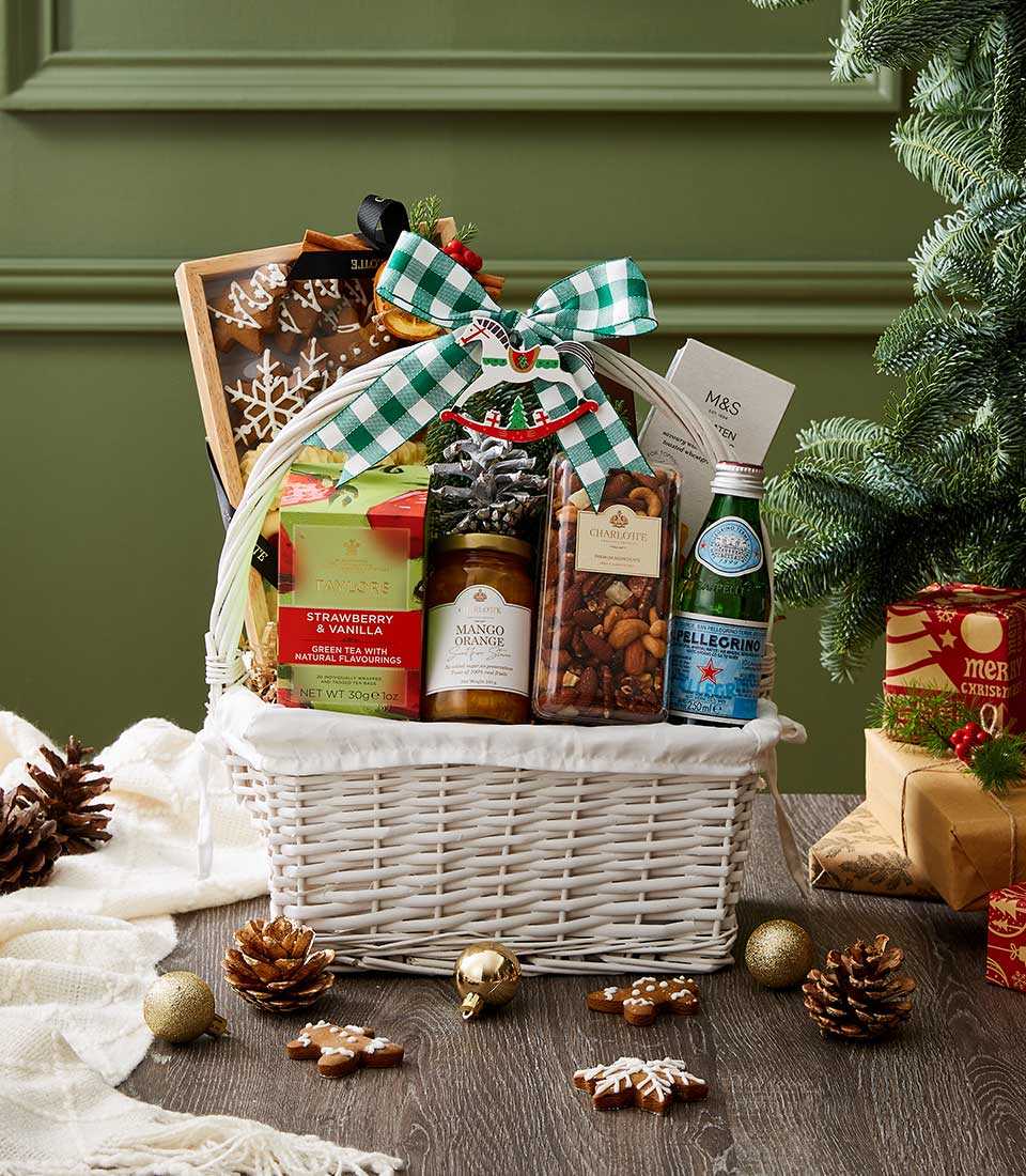 Festive white wicker Christmas hamper with tea, nuts, gingerbread, and preserves tied with green ribbon