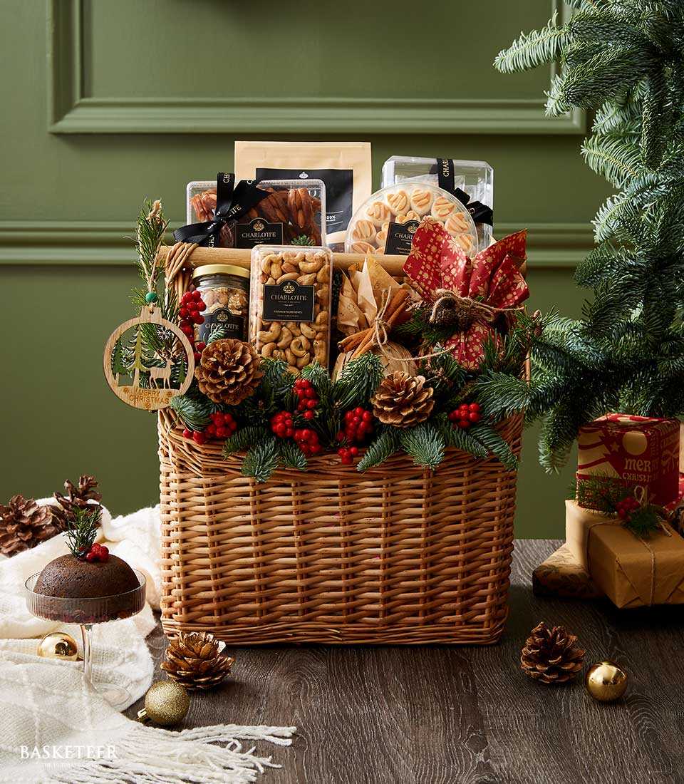 Premium gourmet Christmas gift basket with wicker, pine garland, red berries, pinecones, and festive gold bow