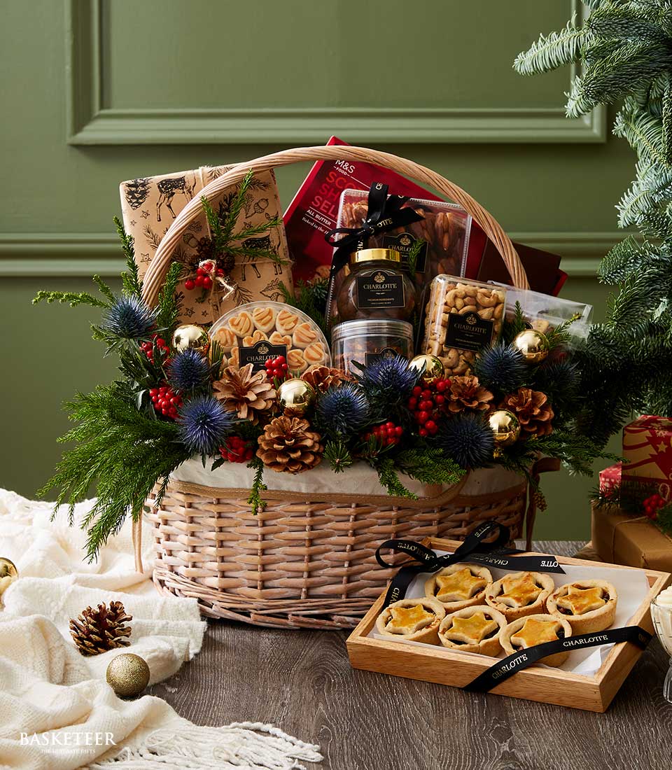 Festive wicker hamper overflowing with gourmet chocolates, Scottish shortbread, nuts, and holiday treats surrounded by pine,
