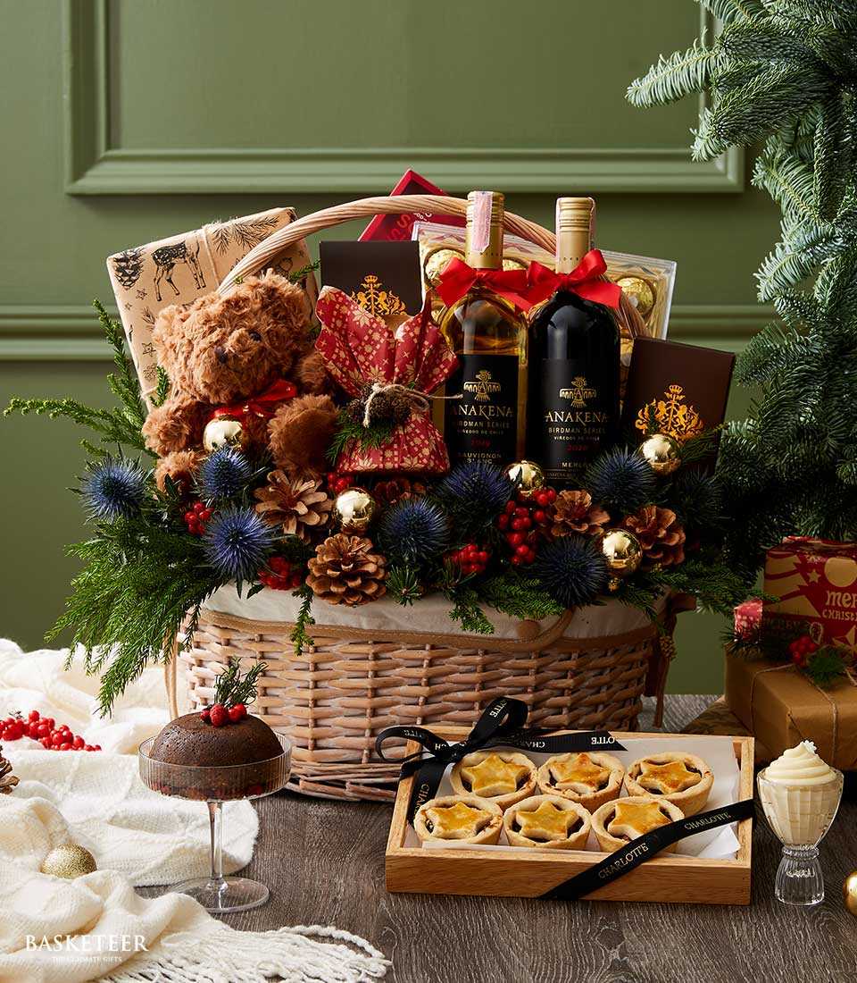 Premium wicker Christmas basket with red and white wine, teddy bear, pinecones, gold ornaments, and festive woodland décor