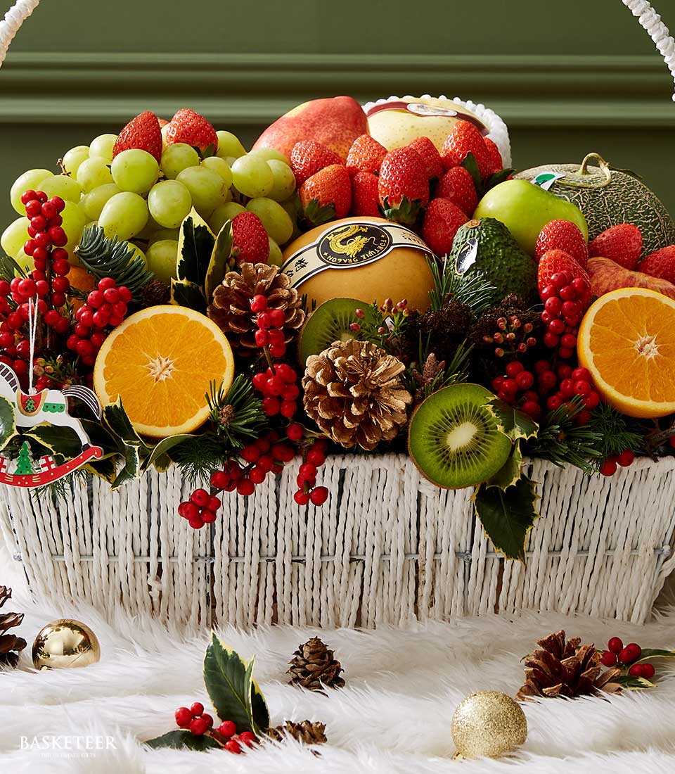 Festive holiday fruit basket with fresh grapes, strawberries, oranges, and kiwis in white woven basket with Christmas