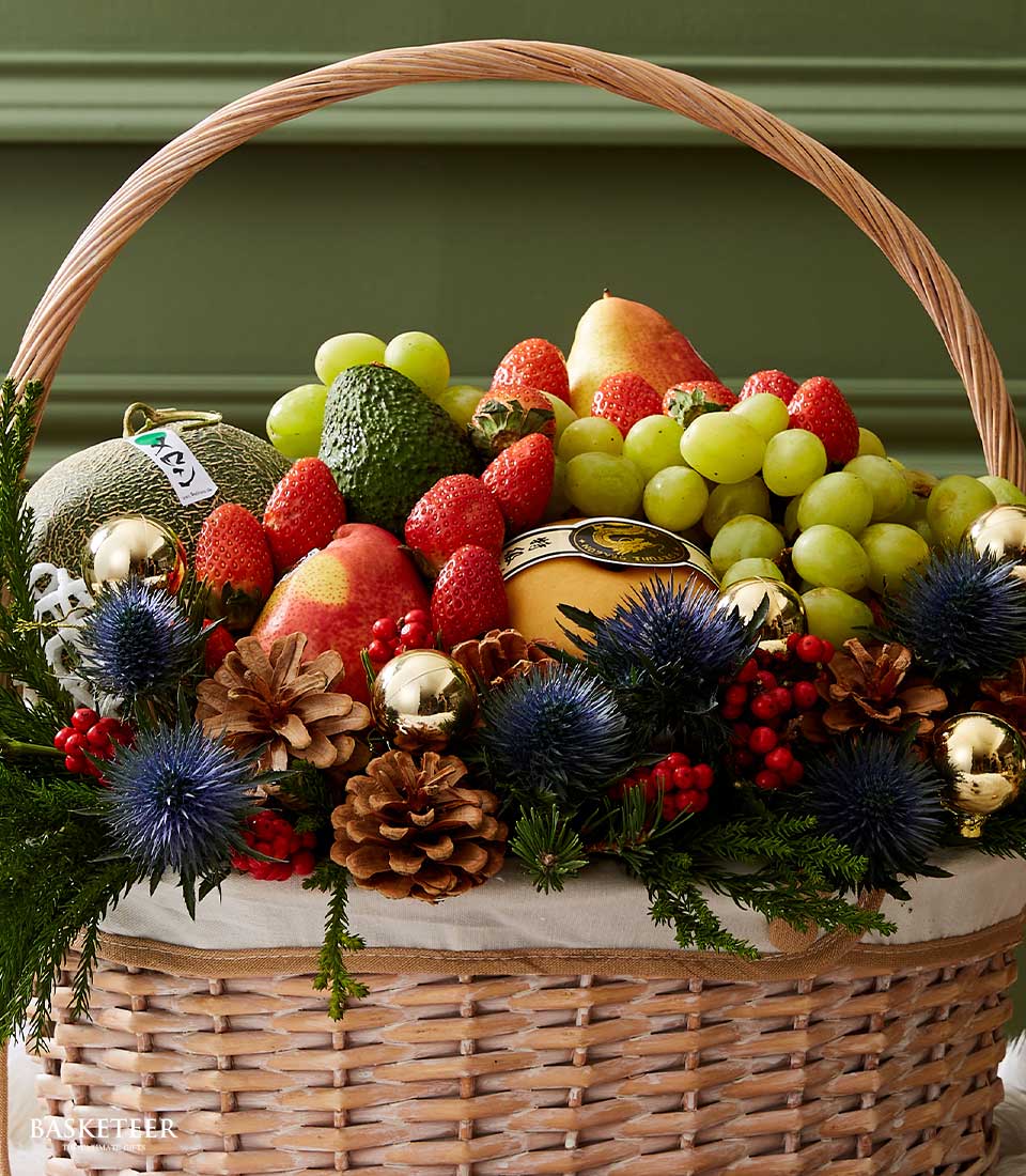 Wicker Christmas fruit basket with grapes, strawberries, melon, pear, cheese, thistle flowers, pinecones, and gold ornaments