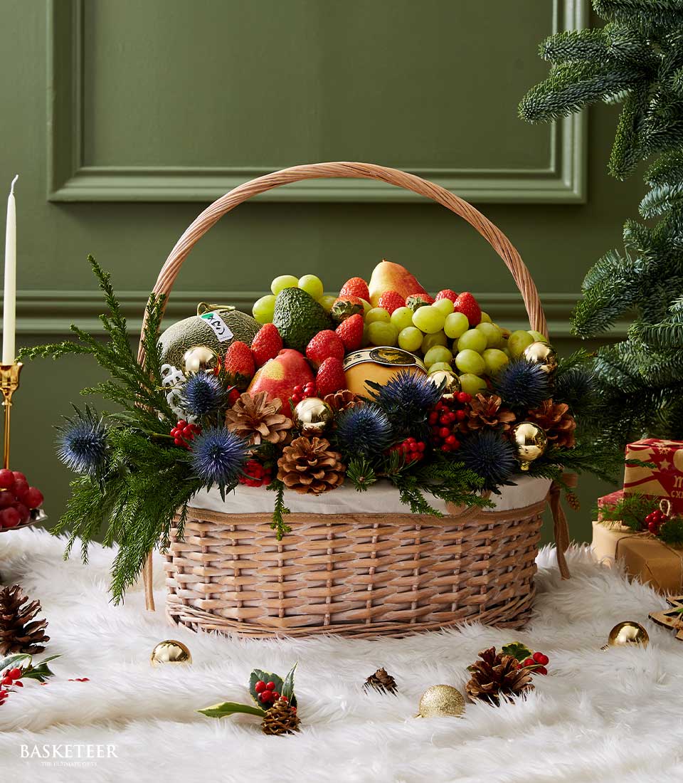 Wicker holiday fruit basket with fresh grapes, strawberries, melon and pear, dressed with evergreen, red berries and gold