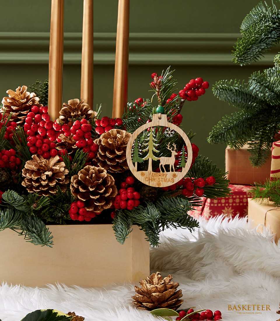 Golden candle pinecone centerpiece with red berries, green pine branches, and wooden ornaments in light wood box