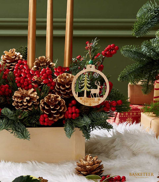 Golden candle pinecone centerpiece with red berries, green pine branches, and wooden ornaments in light wood box