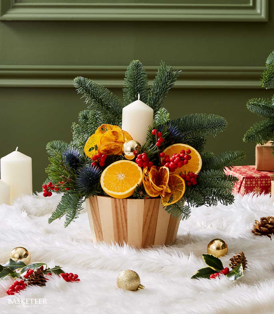 Rustic citrus Christmas centerpiece with white candle, fresh fir, orange slices and red berries in wooden bowl