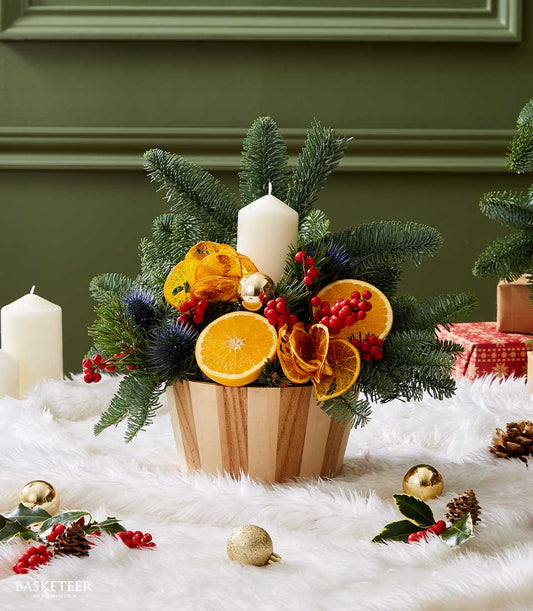 Rustic citrus Christmas centerpiece with white candle, fresh fir, orange slices and red berries in wooden bowl