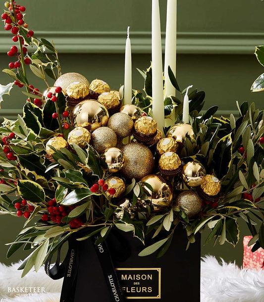Golden Christmas centerpiece with holly, olive branches, gold ornaments, Ferrero Rocher, and white candles in black gift box