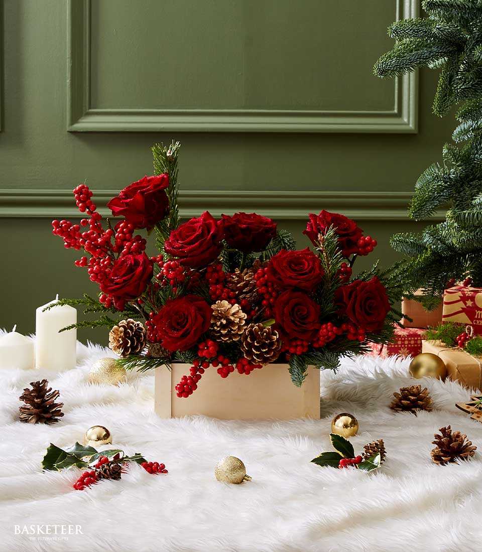 Deep red roses and berries in wooden box with pinecones, festive Christmas floral arrangement