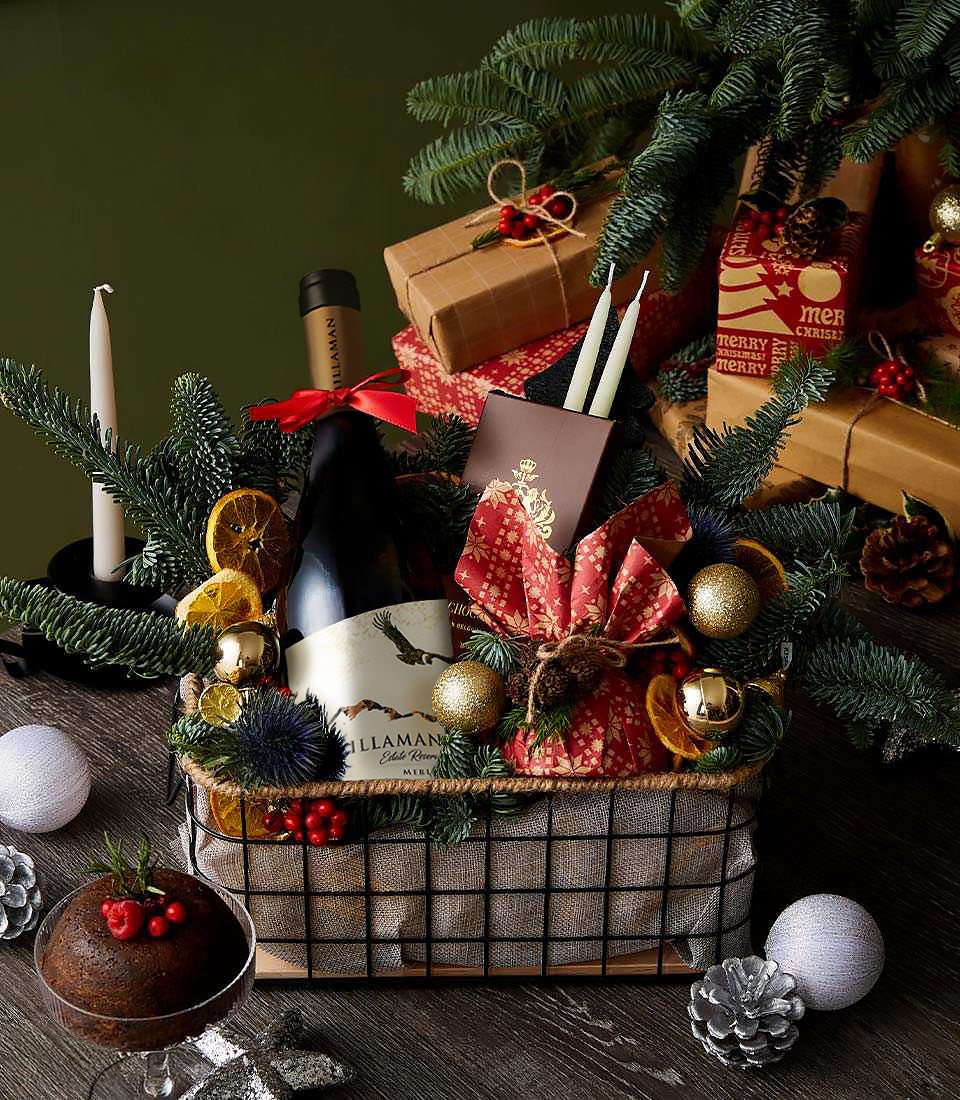 Merlot wine festive gourmet basket with dried citrus, gold baubles, and holiday greenery on dark wood