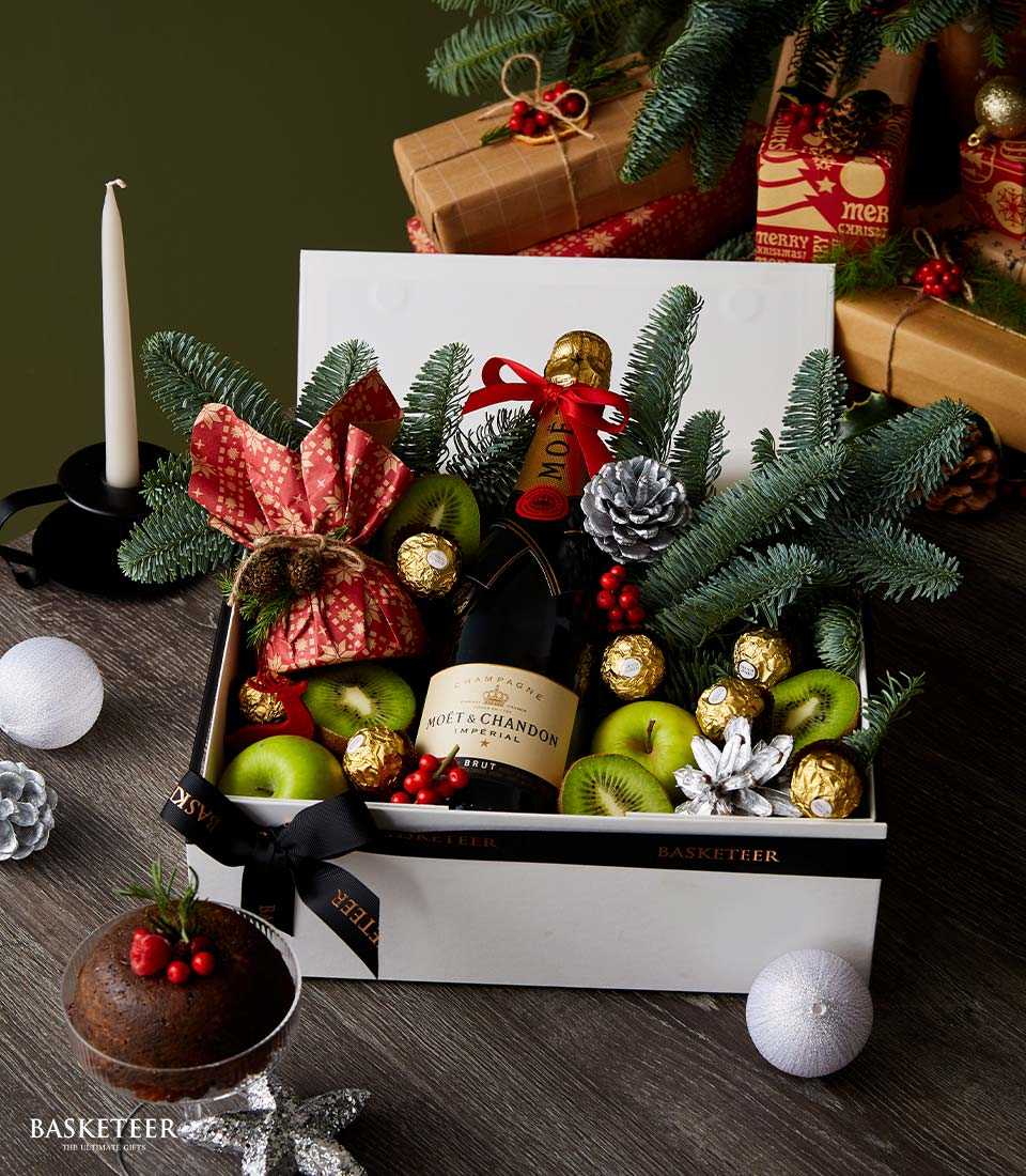 Champagne Christmas gift box with fresh fruit, chocolates, and holiday greenery in luxury presentation