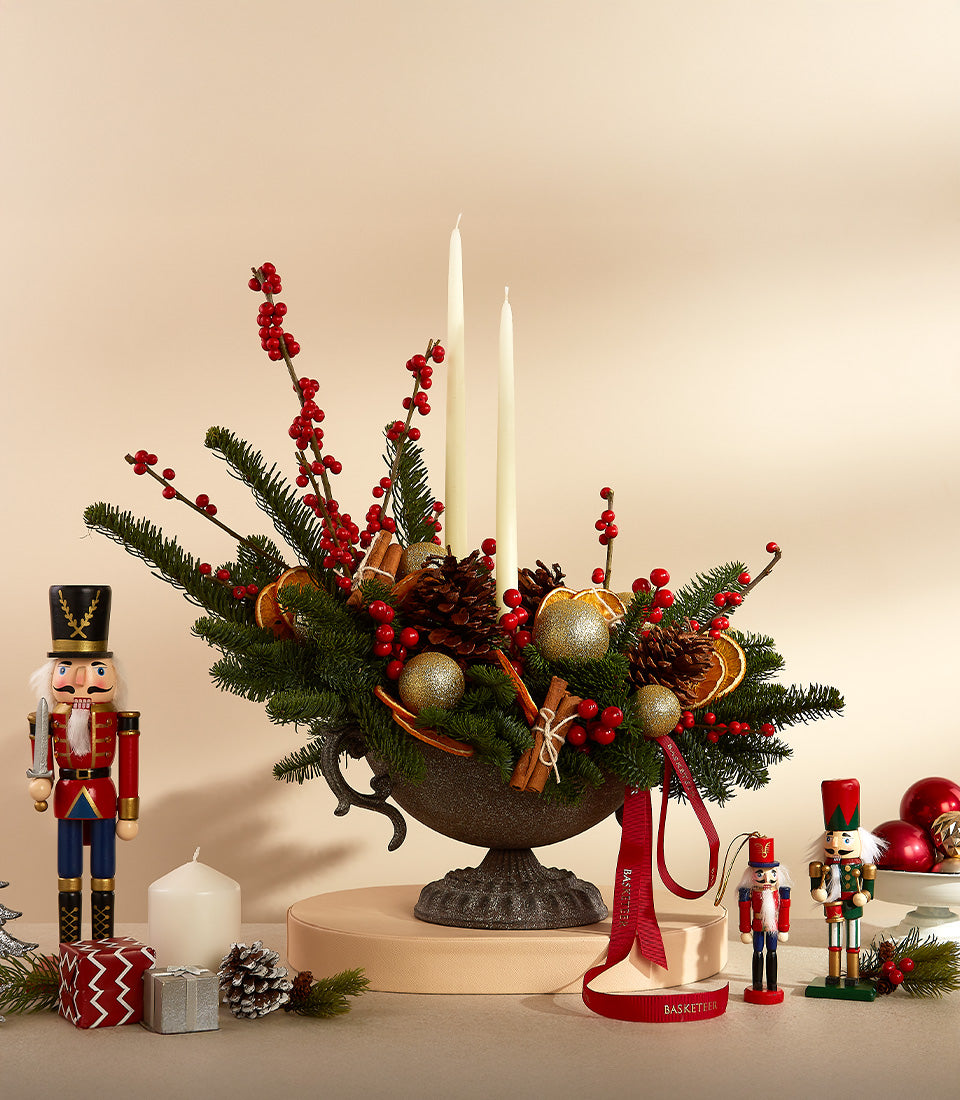 Festive bronze urn with Christmas florals, red berries, cinnamon, dried oranges, and gold baubles with white taper candles