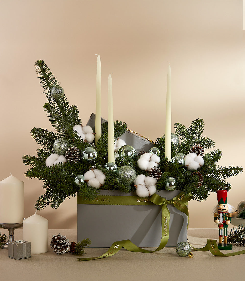 Winter Forest holiday centerpiece with evergreens, silver ornaments, pinecones, cotton bolls, and cream taper candles