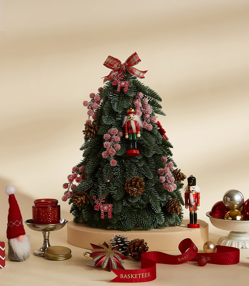 Festive tabletop Christmas tree with nutcracker, red berry clusters, plaid ribbon bow, and coordinating holiday ornaments
