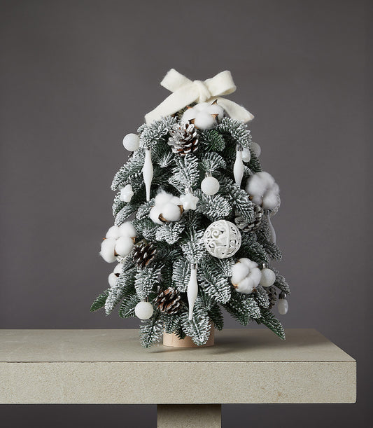 Snowy white flocked Christmas tree with cotton, pinecones, and cream bow ornaments