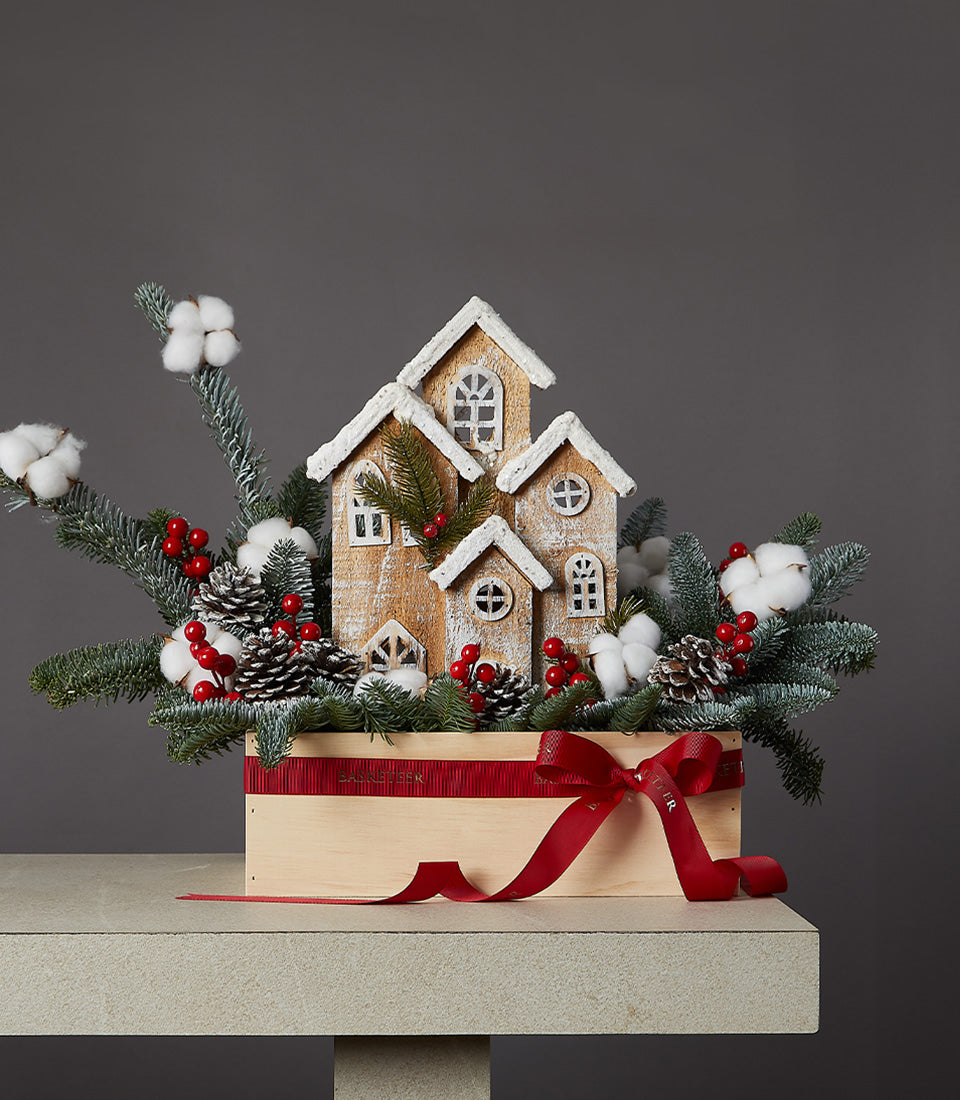 Snowy village Christmas centerpiece with miniature wooden houses, frosted evergreens, and red berries in wooden box